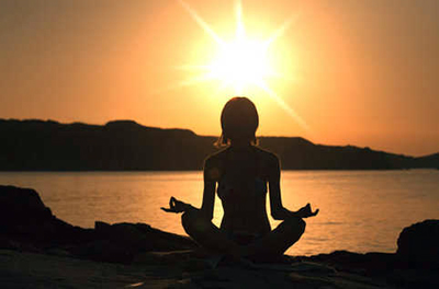 Image d'une femme en position de yoga devant la mer au coucher du soleil